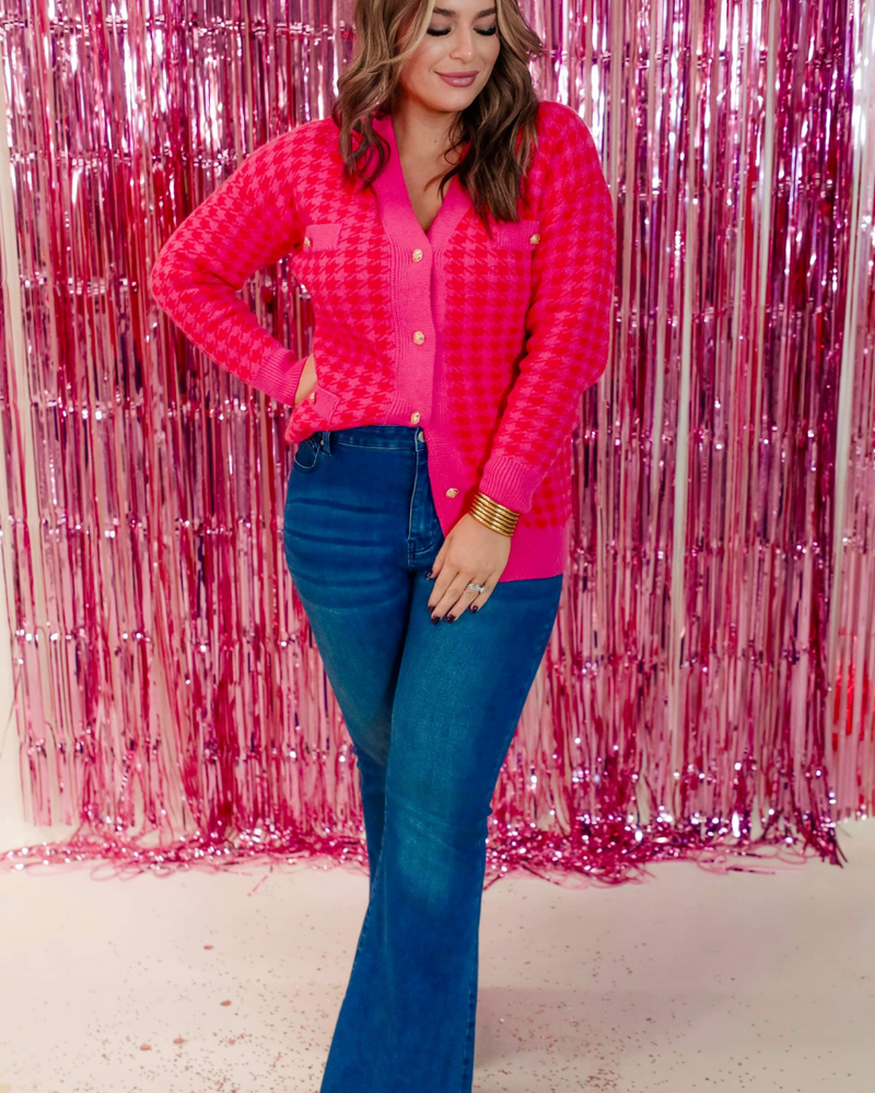 a long-sleeve jacket in a bold pink and red houndstooth pattern with gold detailed buttons, four imitation front pockets, and ribbed classic V-neckline, cuffs, and hemline