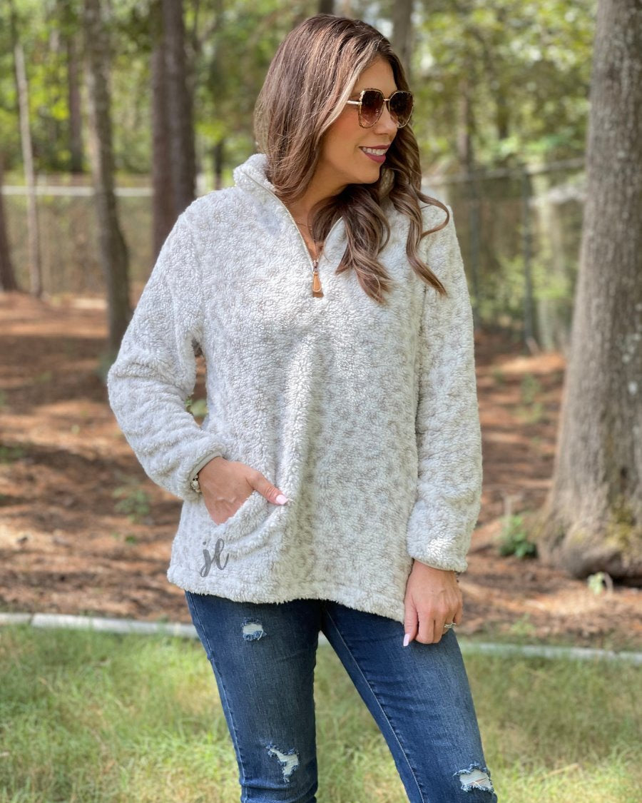 a long-sleeve fluffy pullover with a quarter zip, convenient front pockets, and a foldable collar on a neutral leopard print sherpa fabric