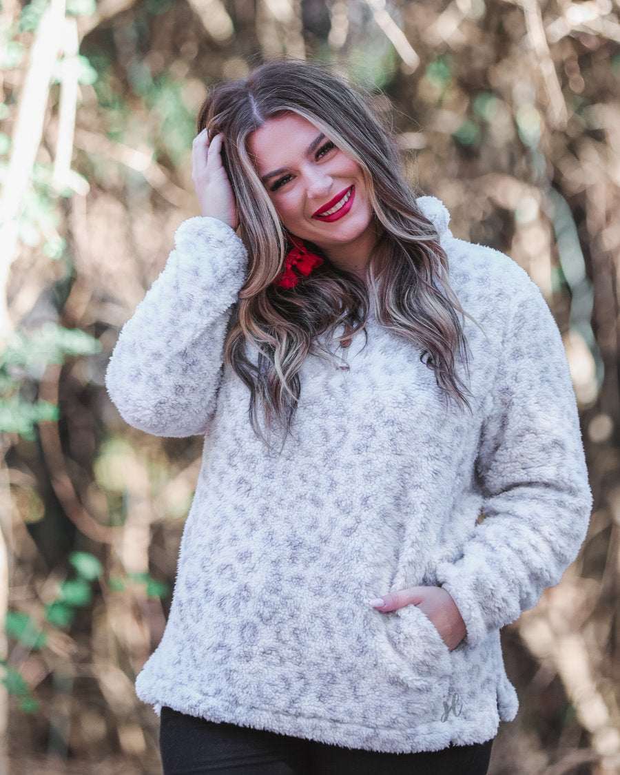 a long-sleeve fluffy pullover with a quarter zip, convenient front pockets, and a foldable collar on a neutral leopard print sherpa fabric