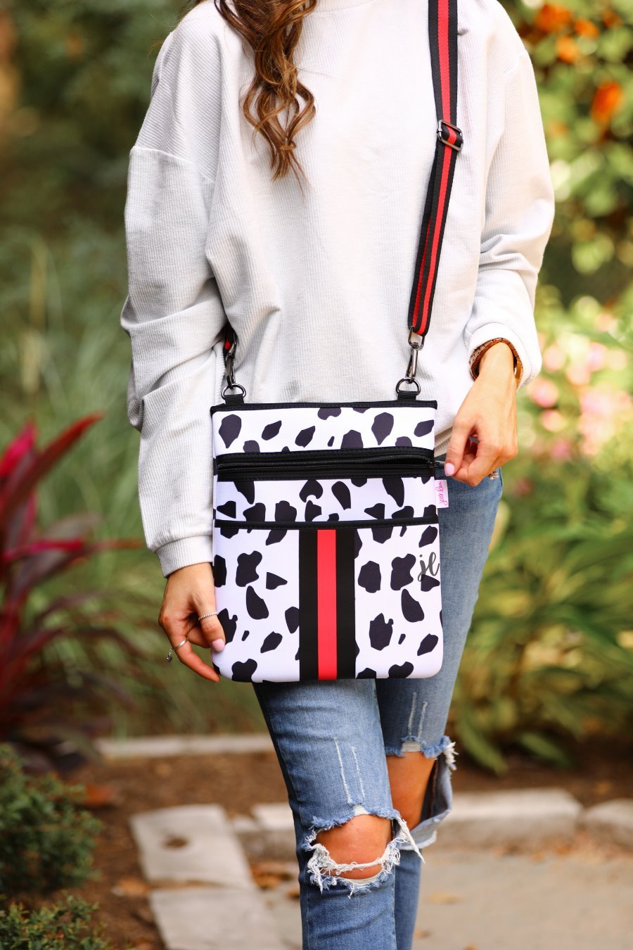 black and ivory dalmation print pattern crossbody bag made of neoprene with perfectly matched signature striped (black and red) adjustable straps and racing stripes with two front pockets (one zip, one open)