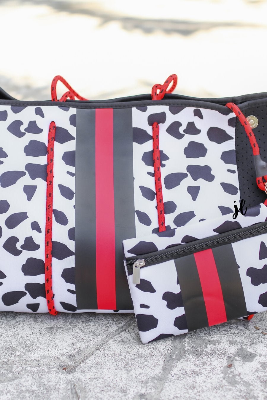 ultra-lightweight tote made of neoprene with removable hard bottom liner, paracord shoulder straps, removable matching zippered pouch, magnetic side snap closures in silver hardware, black interior (tote and pouch), and racing stripes (black and red) on black and red dalmation print pattern