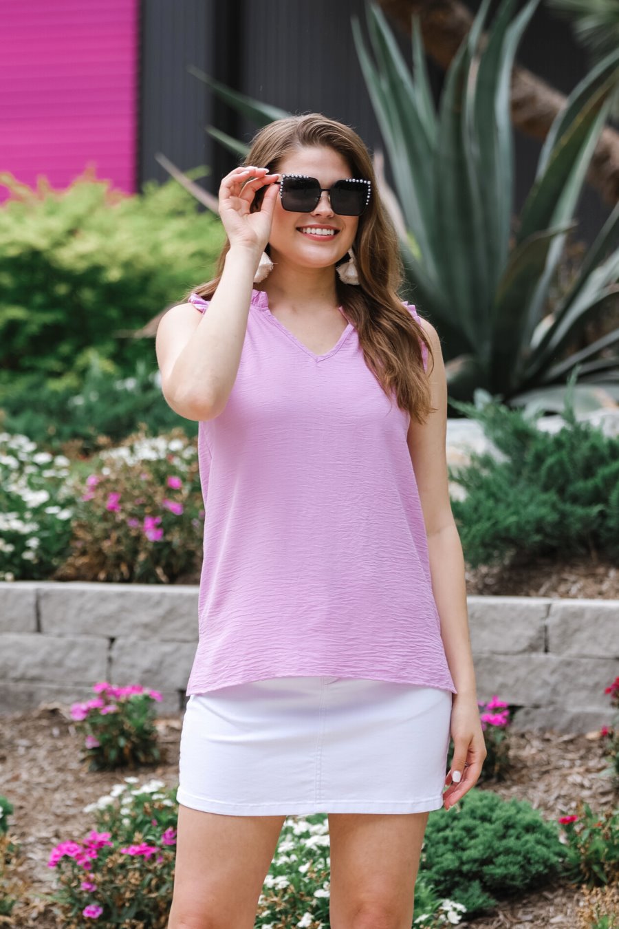 a lavender sleeveless woven top with ruffle trim, a V-neckline, side slits, and a relaxed non-stretch fit