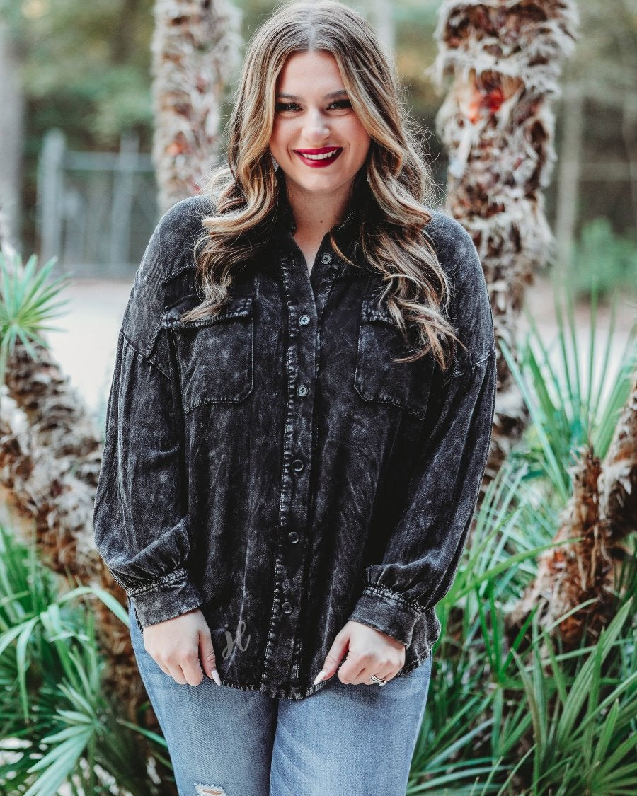 loose long-sleeve top made of soft lightweight material with a button up front, a collared neckline, button closure cuffs, two oversized accent chest pockets, and a slouched silhouette that falls into a rounded hemline with an oversized fit on an acid-washed colored fabric in black