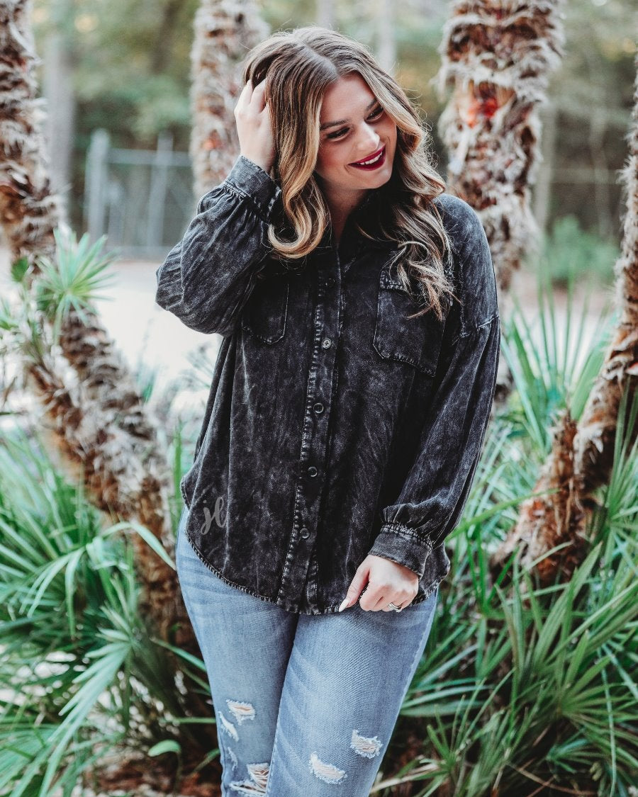 loose long-sleeve top made of soft lightweight material with a button up front, a collared neckline, button closure cuffs, two oversized accent chest pockets, and a slouched silhouette that falls into a rounded hemline with an oversized fit on an acid-washed colored fabric in black