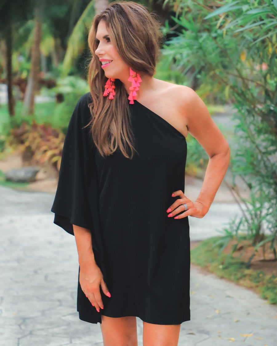 a black asymmetrical one-shoulder dress made of lightweight fabric with a stretchy elastic neckline, breezy silhouette, draped sleeve, and a clean straight hemline
