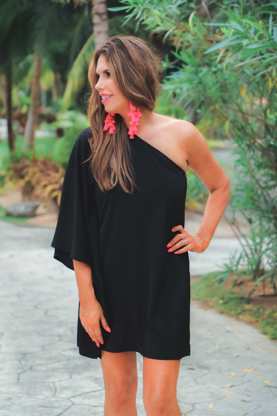 a black asymmetrical one-shoulder dress made of lightweight fabric with a stretchy elastic neckline, breezy silhouette, draped sleeve, and a clean straight hemline