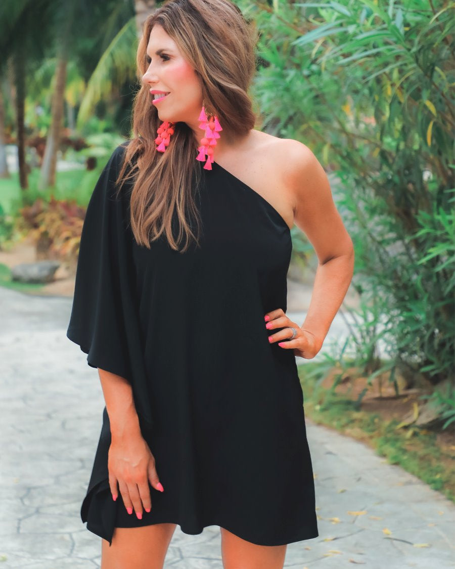 a black asymmetrical one-shoulder dress made of lightweight fabric with a stretchy elastic neckline, breezy silhouette, draped sleeve, and a clean straight hemline