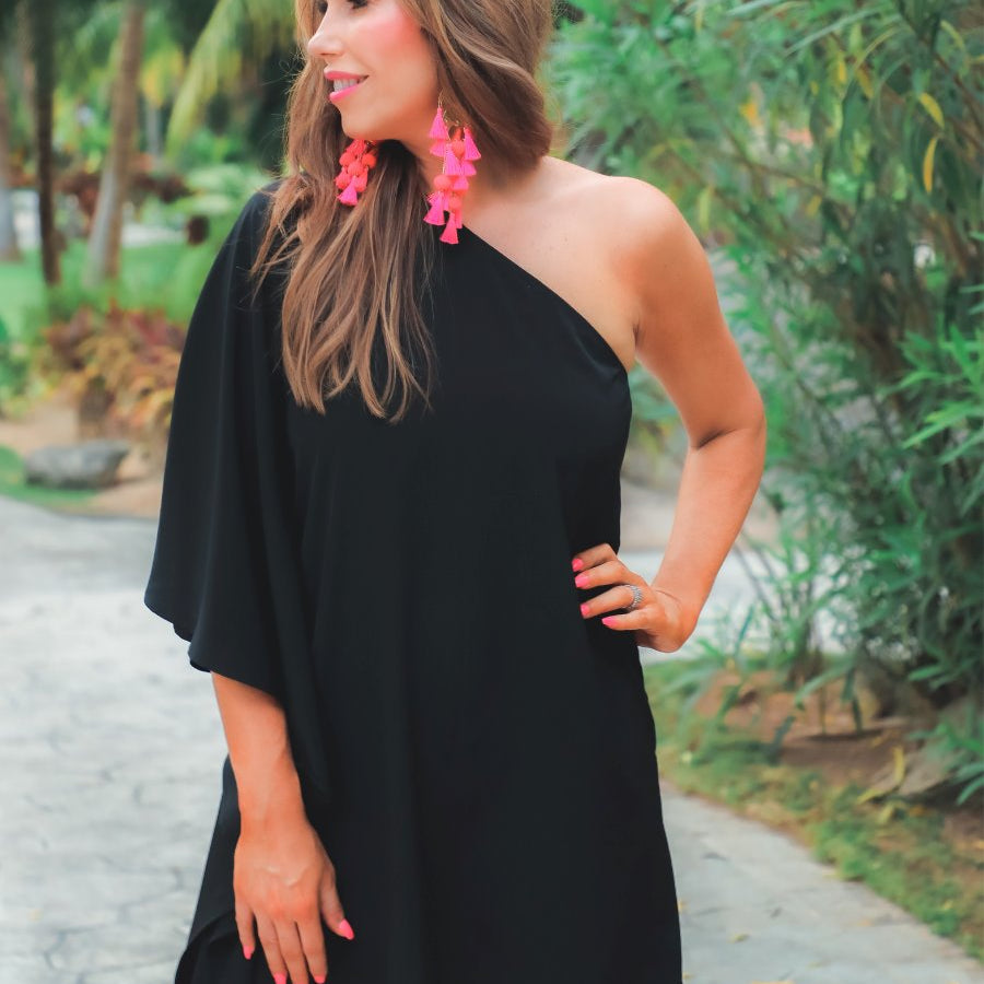 a black asymmetrical one-shoulder dress made of lightweight fabric with a stretchy elastic neckline, breezy silhouette, draped sleeve, and a clean straight hemline