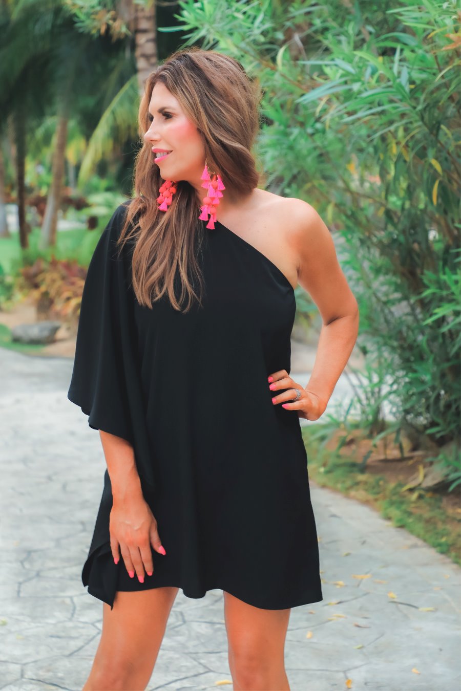 a black asymmetrical one-shoulder dress made of lightweight fabric with a stretchy elastic neckline, breezy silhouette, draped sleeve, and a clean straight hemline