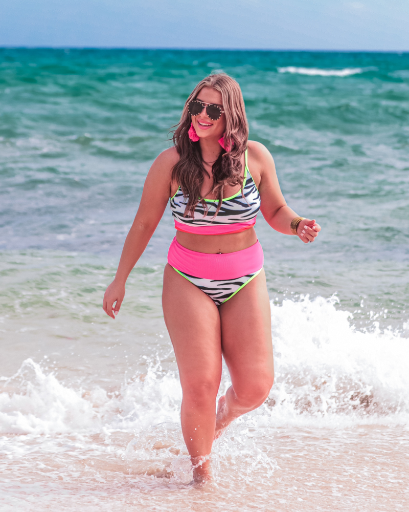 two-piece swimsuit made of stretchy patterned material with a bralette style top, adjustable neon green spaghetti straps, removable padding, and ending in full coverage high-waisted bottoms with a contrasting neon pink band and green trim