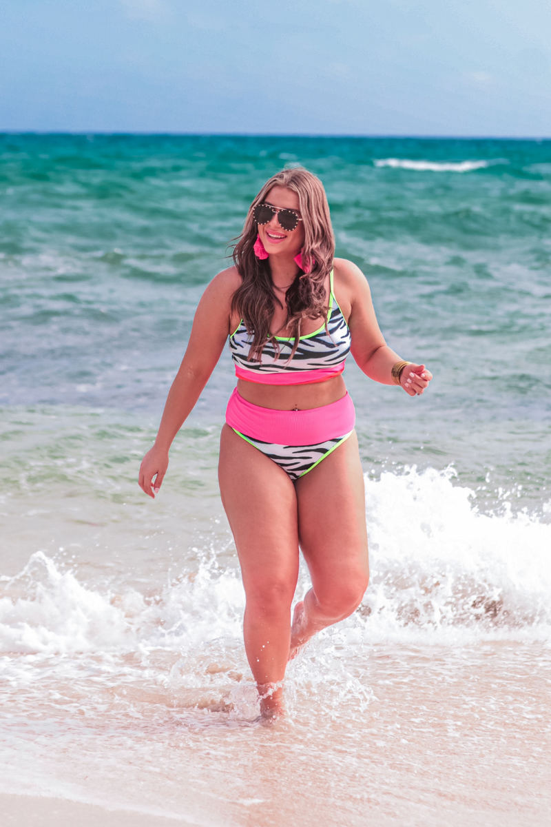 two-piece swimsuit made of stretchy patterned material with a bralette style top, adjustable neon green spaghetti straps, removable padding, and ending in full coverage high-waisted bottoms with a contrasting neon pink band and green trim