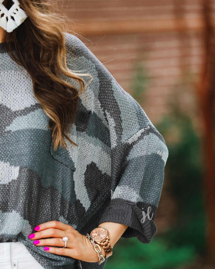 three-quarter cuffed sleeve unlined sweater crafted from a loose knit material with an oversized fit, a rounded neckline, a chest pocket, and trim on the collar, hem, and pocket on a grey camouflage pattern and charcoal base