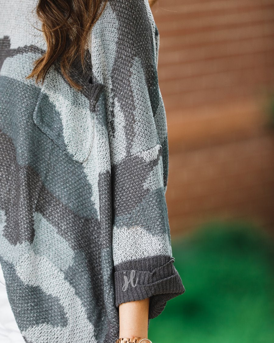 three-quarter cuffed sleeve unlined sweater crafted from a loose knit material with an oversized fit, a rounded neckline, a chest pocket, and trim on the collar, hem, and pocket on a grey camouflage pattern and charcoal base