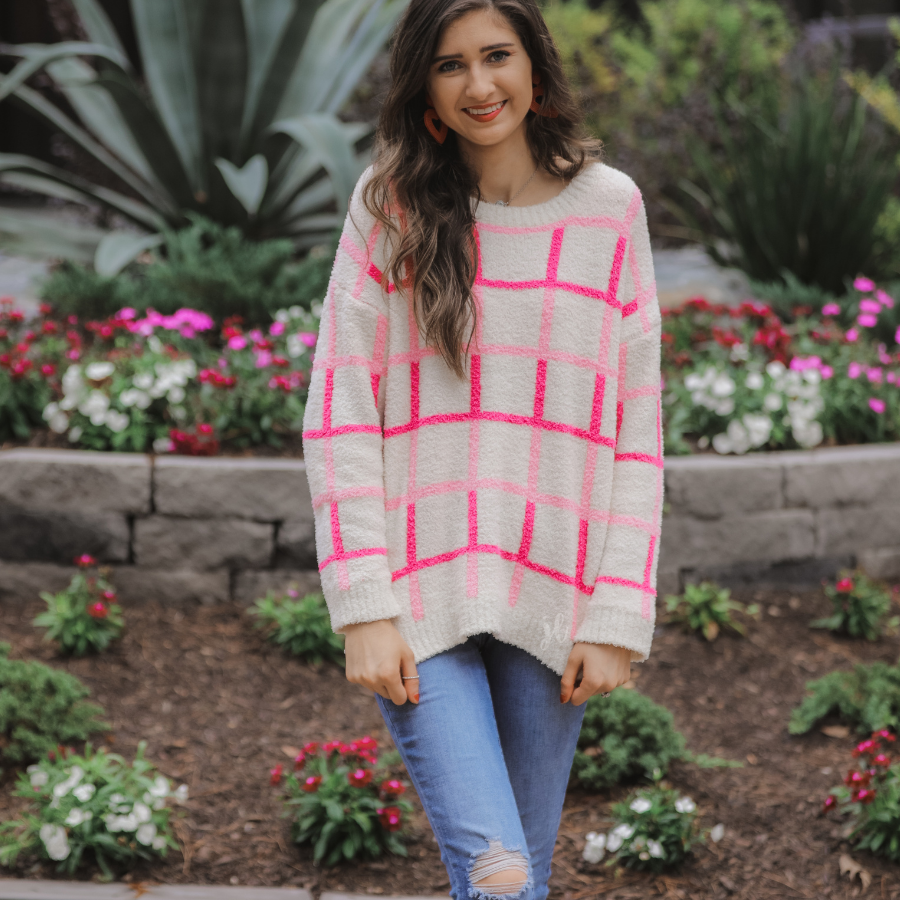 a plush knit long-sleeve sweater with a pink and ivory plaid pattern, relaxed drop-shoulder fit, classic round neckline, and ribbed detailing at the cuffs, sleeves, and hemline for a clean, polished finish