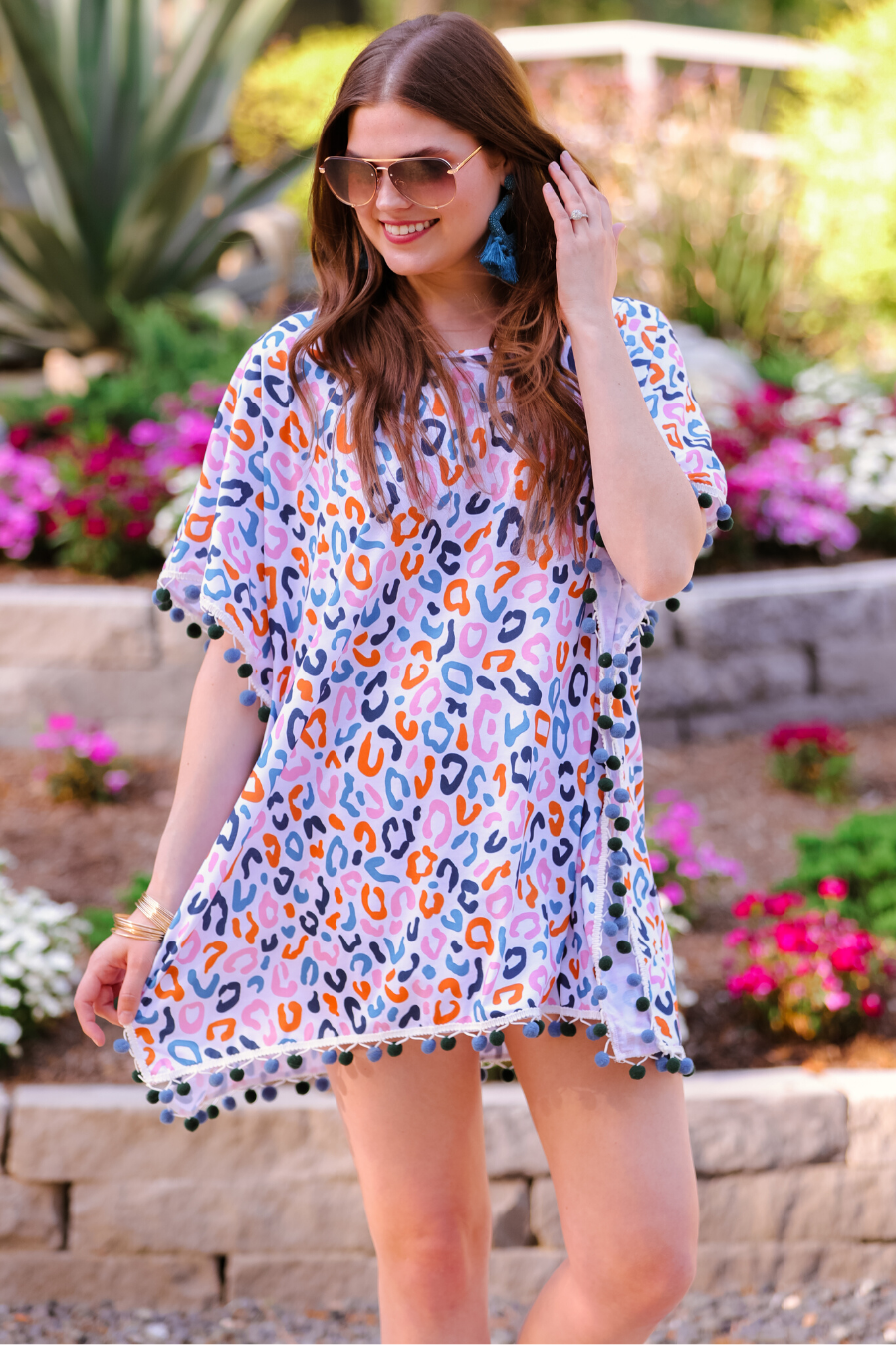 lightweight coverup made of breezy material with alternating dark blue and dark green pom pom decorative trim and multicolor leopard print pattern on a white background
