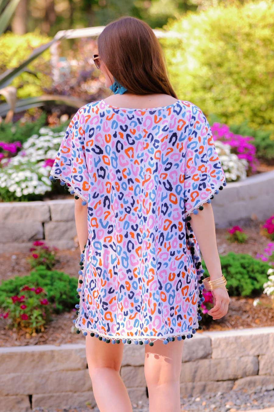 lightweight coverup made of breezy material with alternating dark blue and dark green pom pom decorative trim and multicolor leopard print pattern on a white background