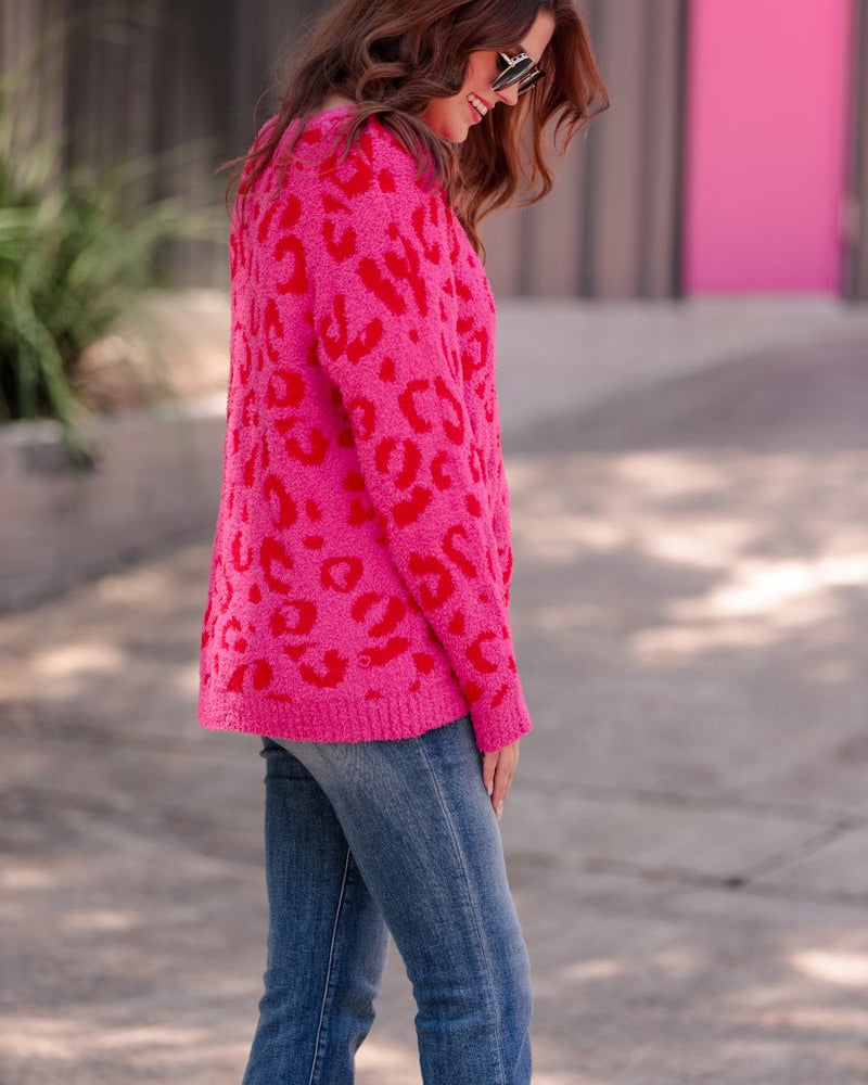 a fuzzy textured long-sleeve sweater with a vibrant pink leopard pattern on a pink base and ribbed detailing on the round neckline, cuffs, and structured hemline
