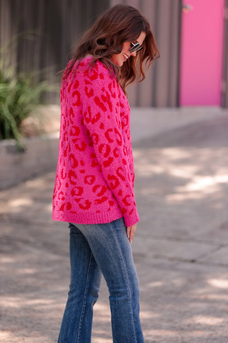 a fuzzy textured long-sleeve sweater with a vibrant pink leopard pattern on a pink base and ribbed detailing on the round neckline, cuffs, and structured hemline