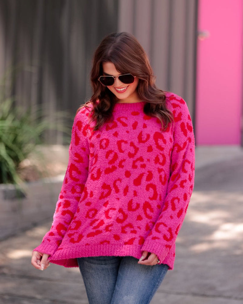a fuzzy textured long-sleeve sweater with a vibrant pink leopard pattern on a pink base and ribbed detailing on the round neckline, cuffs, and structured hemline