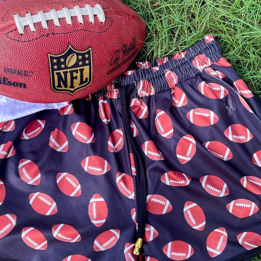 mid-rise relaxed fit activewear shorts with side pockets and a tie waist drawstring with gold bead accent, designed with a football pattern print, black base, and black trim
