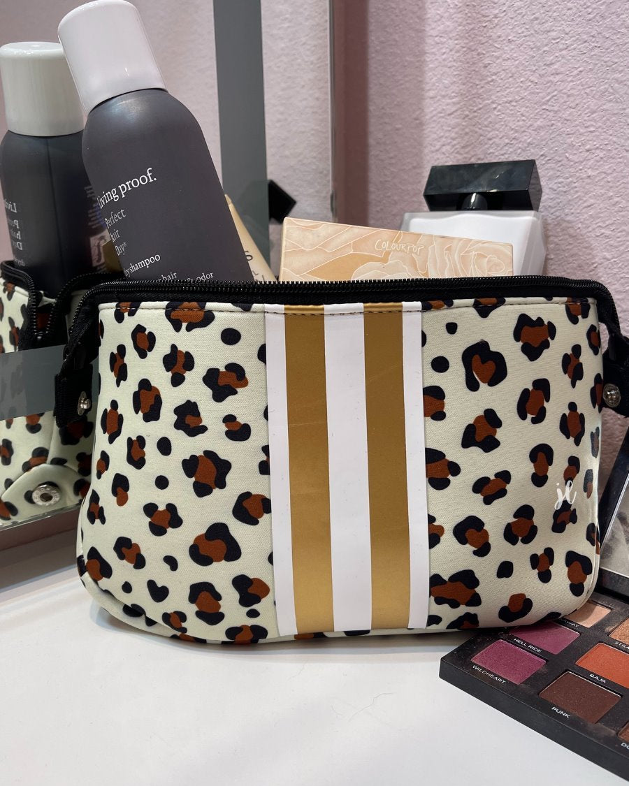 spacious cosmetic bag in a gold leopard print made of neoprene, accentuated with gold and white racing stripe, one top zipper, and side snap closures in silver hardware