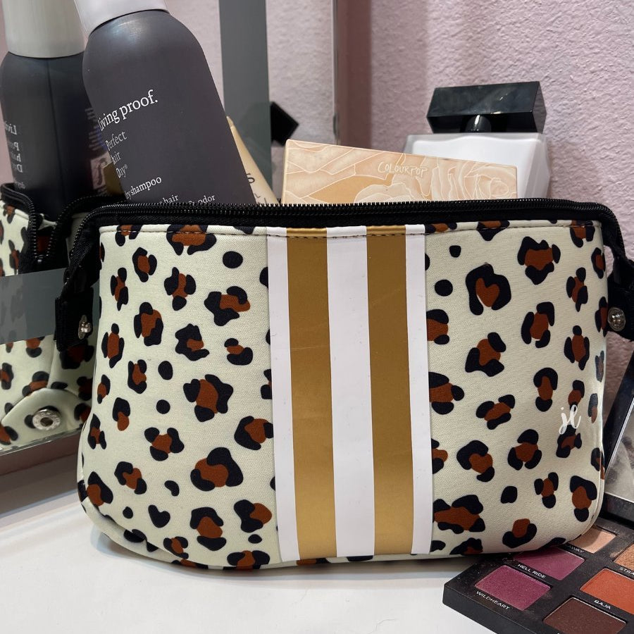 spacious cosmetic bag in a gold leopard print made of neoprene, accentuated with gold and white racing stripe, one top zipper, and side snap closures in silver hardware