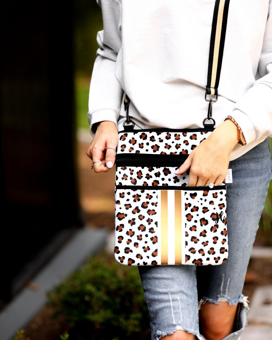 spacious crossbody bag in a gold leopard print made of neoprene with an adjustable strap (black and gold), two front pockets (one zipper, one open), and racing stripes (black and white)