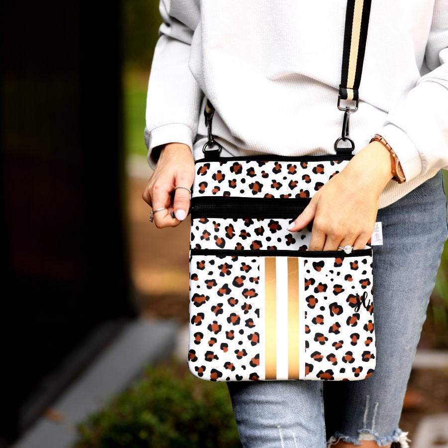 spacious crossbody bag in a gold leopard print made of neoprene with an adjustable strap (black and gold), two front pockets (one zipper, one open), and racing stripes (black and white)