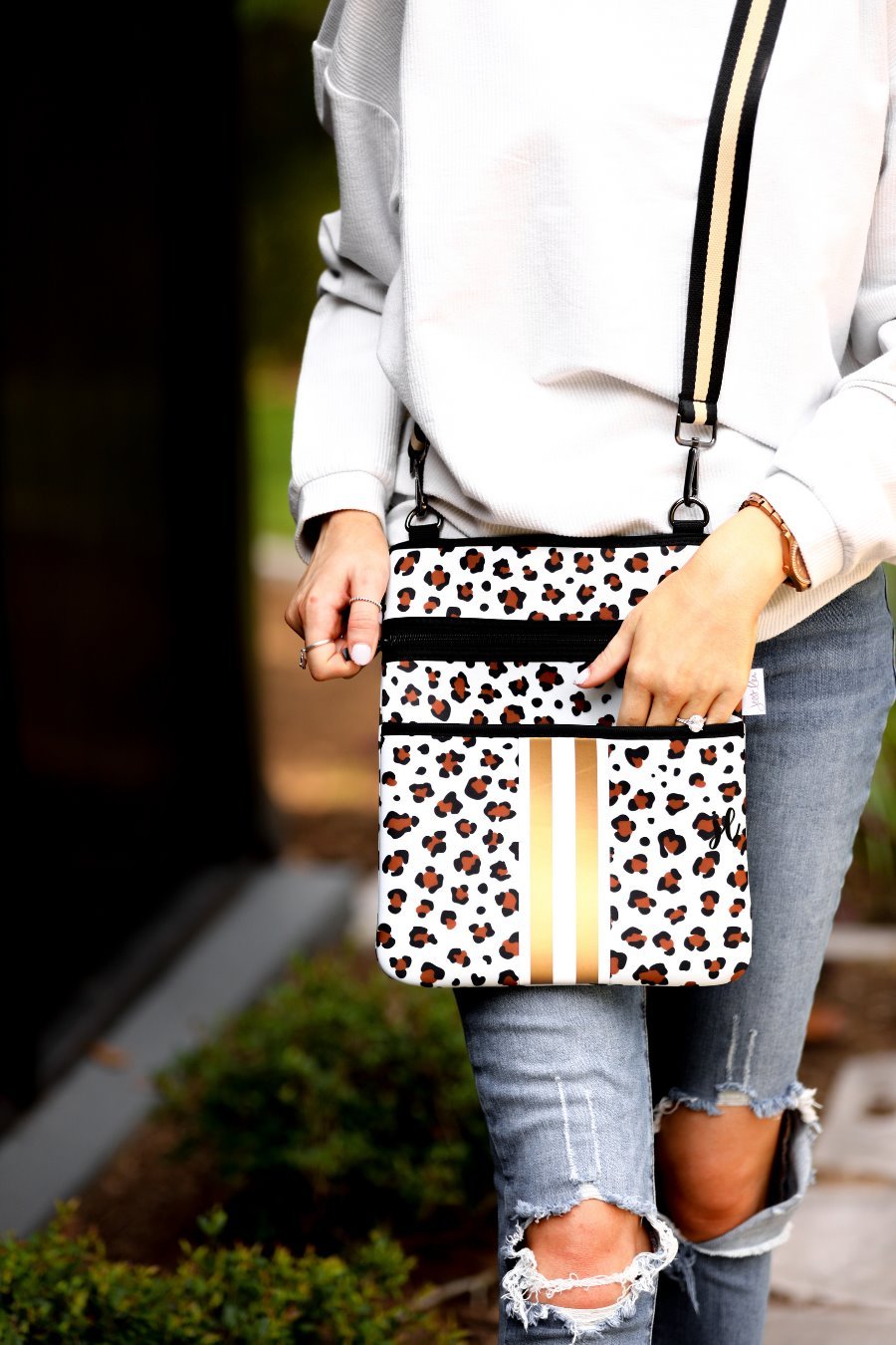 spacious crossbody bag in a gold leopard print made of neoprene with an adjustable strap (black and gold), two front pockets (one zipper, one open), and racing stripes (black and white)