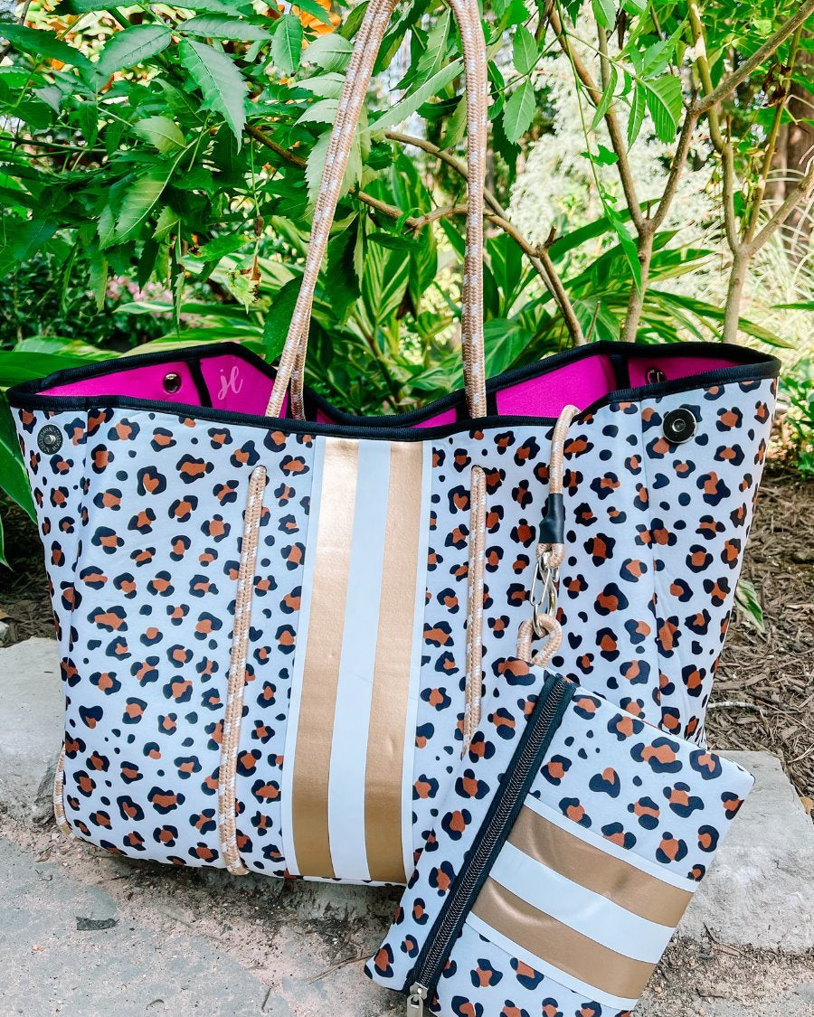 ultra-lightweight tote made of neoprene with a removable hard bottom liner, paracord shoulder straps, removable matching zippered pouch, magnetic side snap closures in silver hardware, hot pink interior (tote and pouch), and racing stripes (gold and white) on a brown and black leopard print pattern