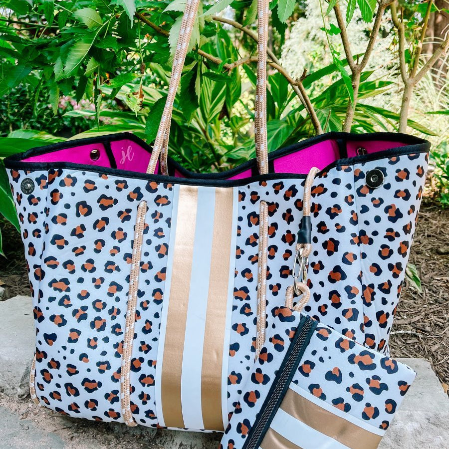 ultra-lightweight tote made of neoprene with a removable hard bottom liner, paracord shoulder straps, removable matching zippered pouch, magnetic side snap closures in silver hardware, hot pink interior (tote and pouch), and racing stripes (gold and white) on a brown and black leopard print pattern