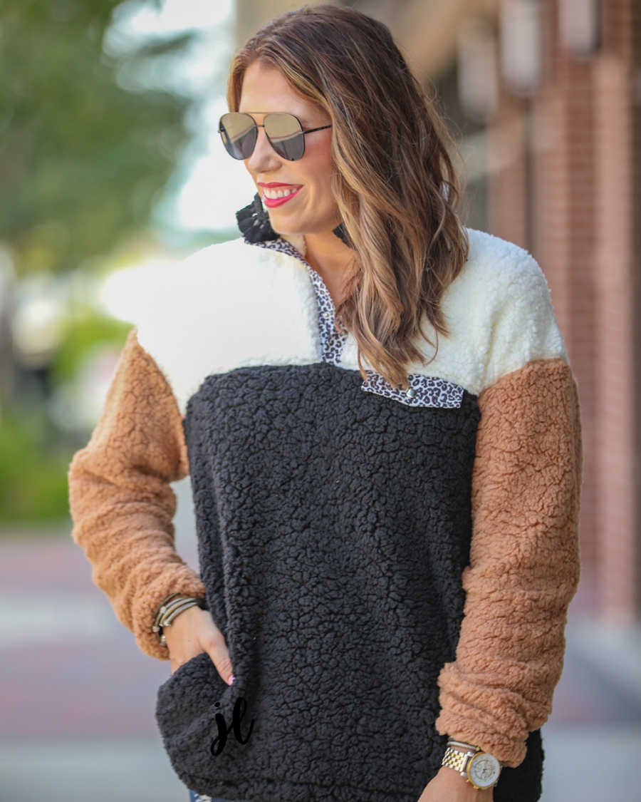 a long-sleeve fluffy pullover with a quarter-leopard snap closure, a faux leopard front chest pocket, a foldable collar, and convenient side pockets on a black, taupe, and white color block fabric that is slightly oversized