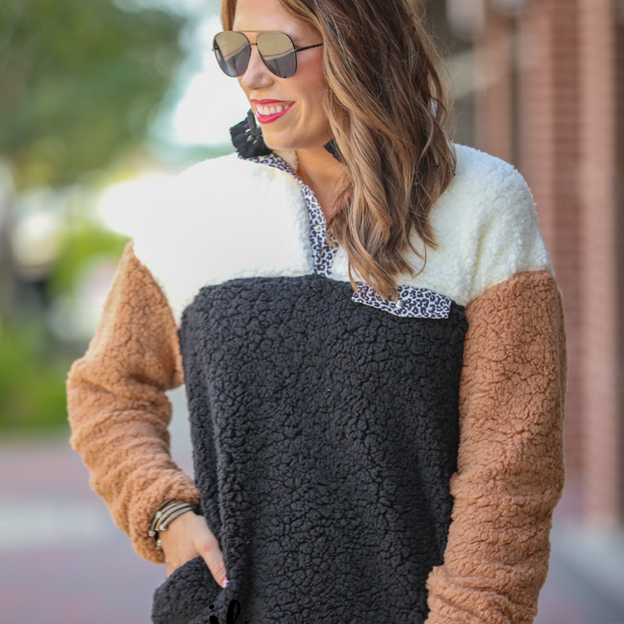 a long-sleeve fluffy pullover with a quarter-leopard snap closure, a faux leopard front chest pocket, a foldable collar, and convenient side pockets on a black, taupe, and white color block fabric that is slightly oversized