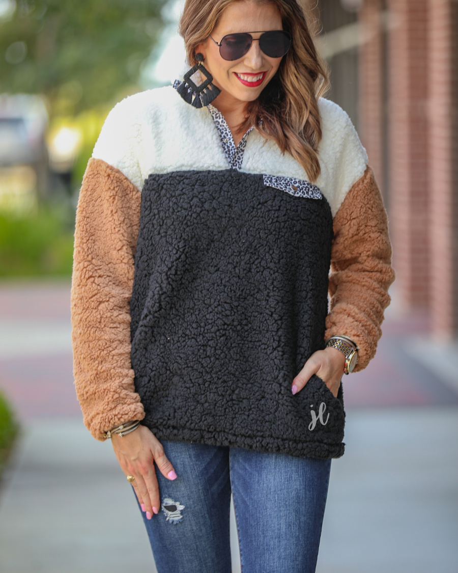 a long-sleeve fluffy pullover with a quarter-leopard snap closure, a faux leopard front chest pocket, a foldable collar, and convenient side pockets on a black, taupe, and white color block fabric that is slightly oversized