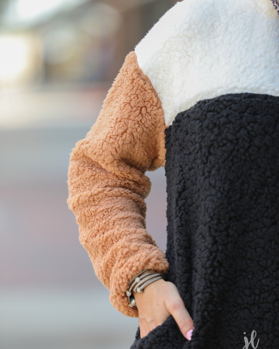 a long-sleeve fluffy pullover with a quarter-leopard snap closure, a faux leopard front chest pocket, a foldable collar, and convenient side pockets on a black, taupe, and white color block fabric that is slightly oversized
