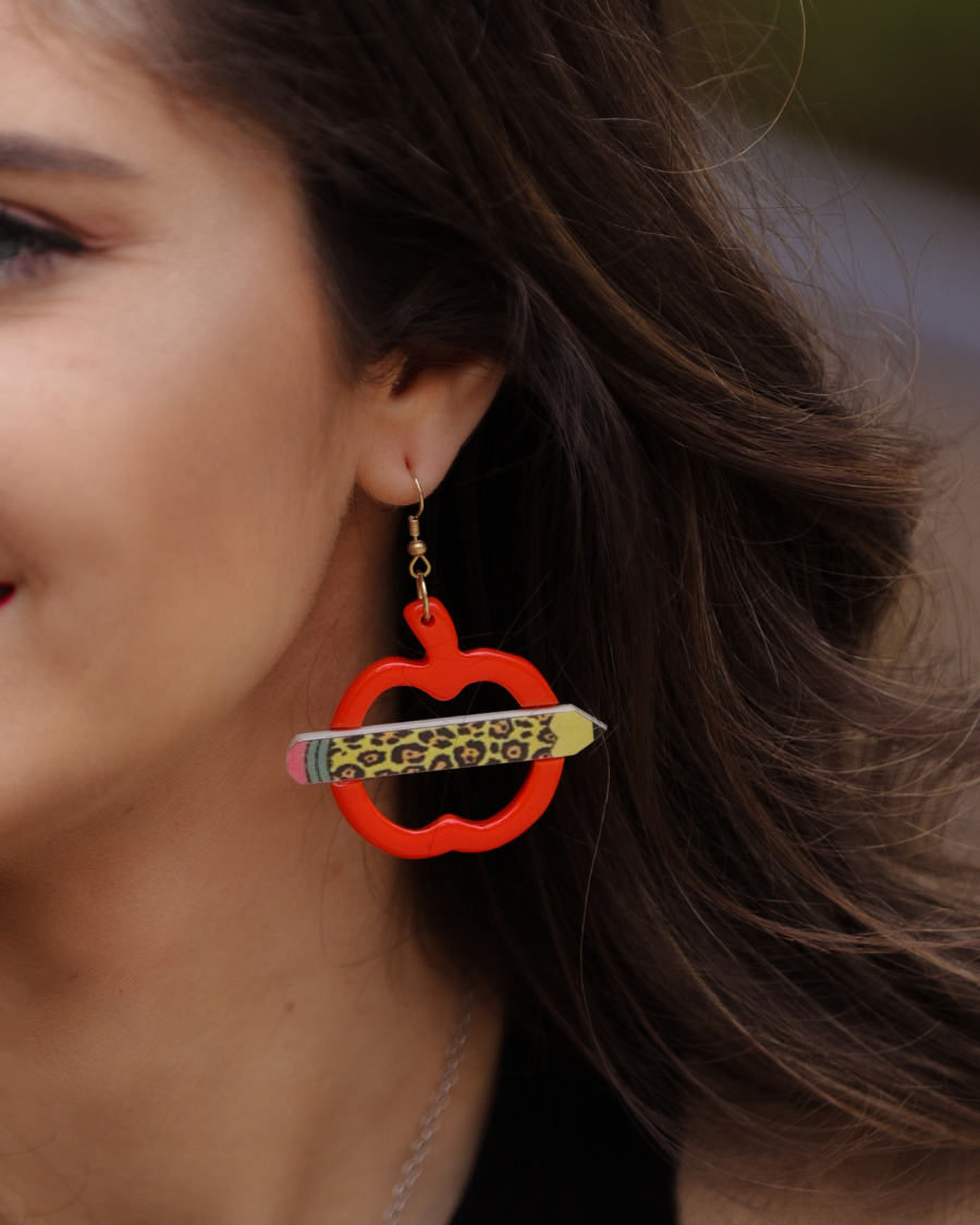 gold fish hook earrings in the shape of an open apple with a leopard pencil pointing outwards