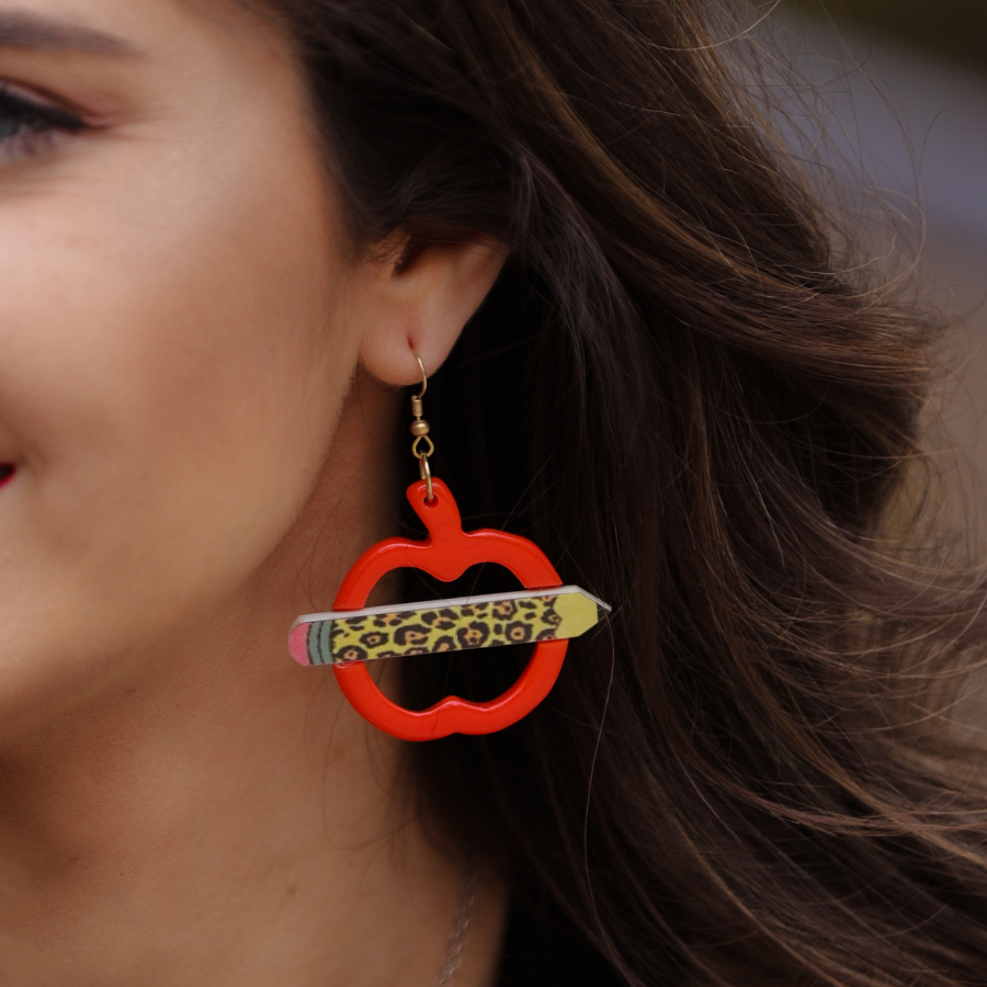 gold fish hook earrings in the shape of an open apple with a leopard pencil pointing outwards