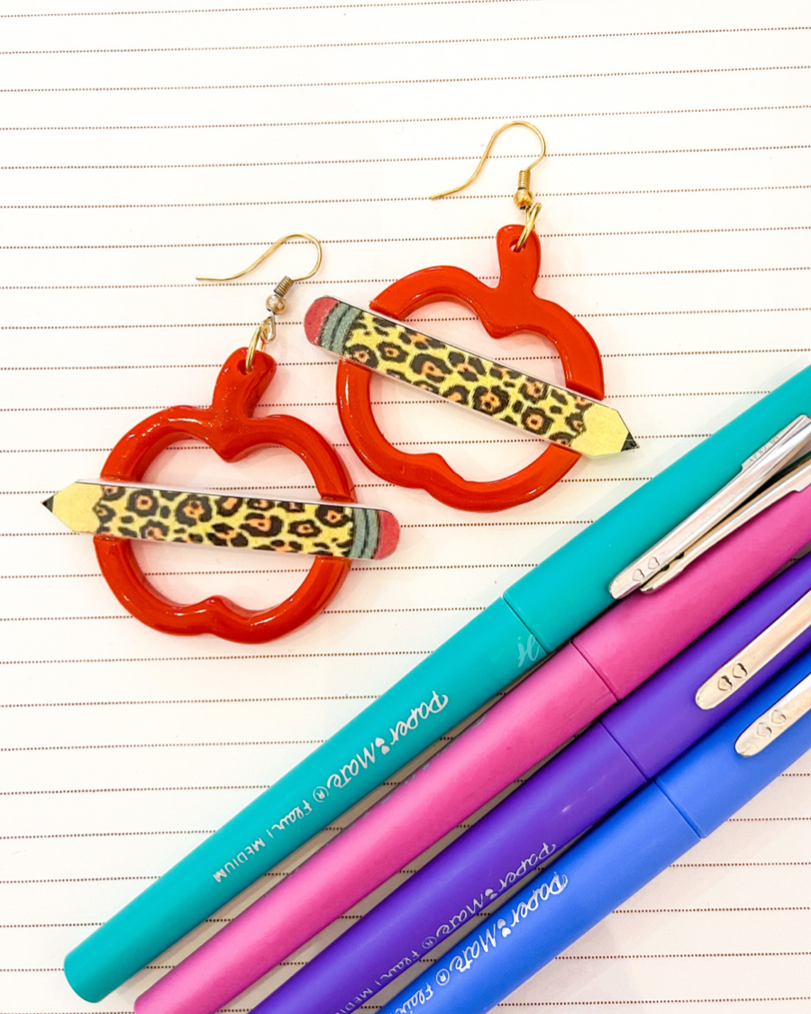 gold fish hook earrings in the shape of an open apple with a leopard pencil pointing outwards