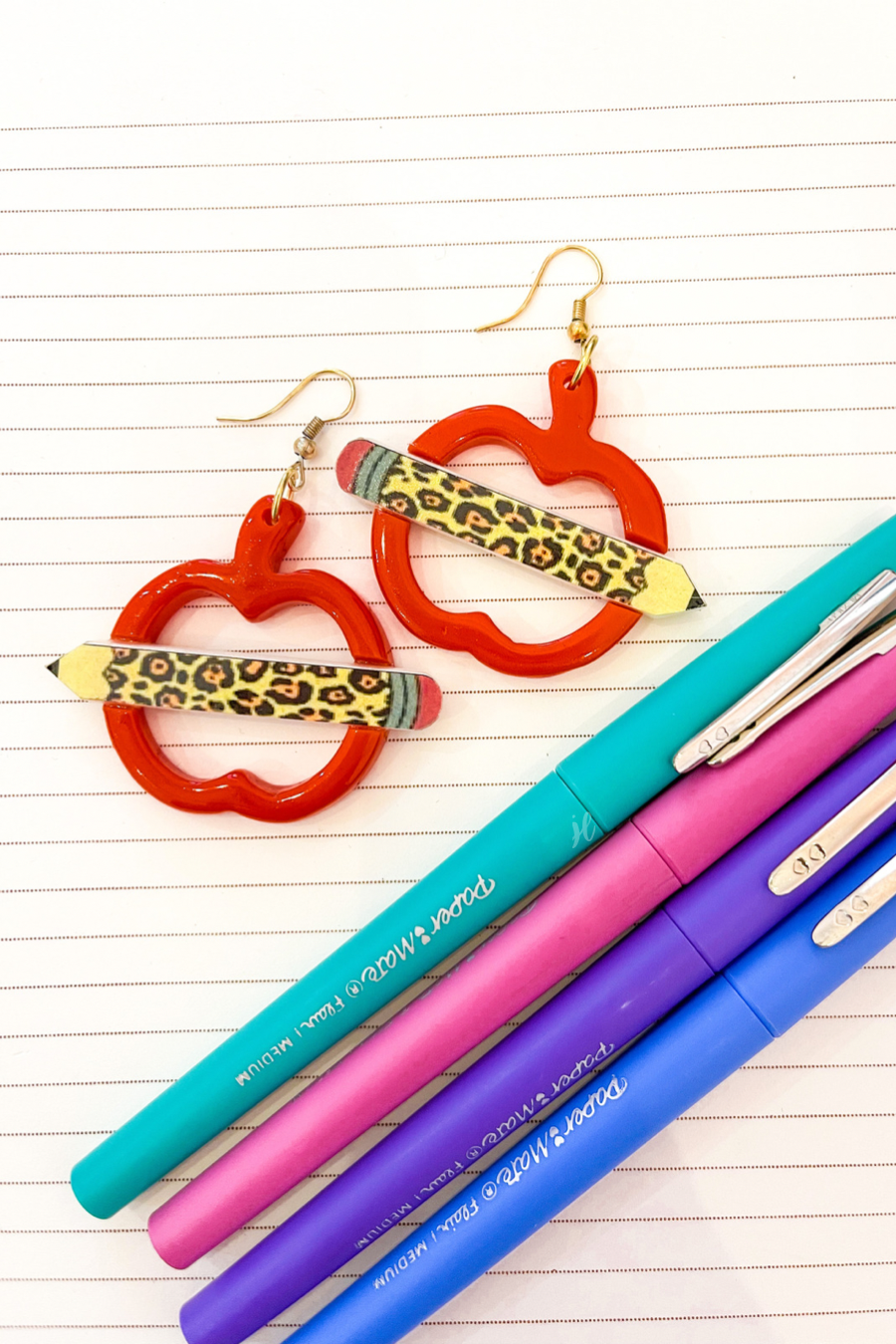 gold fish hook earrings in the shape of an open apple with a leopard pencil pointing outwards