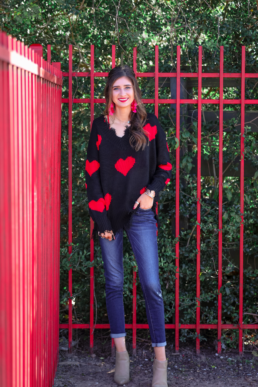 a long-sleeve sweater crafted from ultra soft, stretchy knit fabric with striking red heart motifs across a rich black knit, a relaxed drop-shoulder fit, and distressed ribbed detailing on v-neckline, cuffs, and hemline
