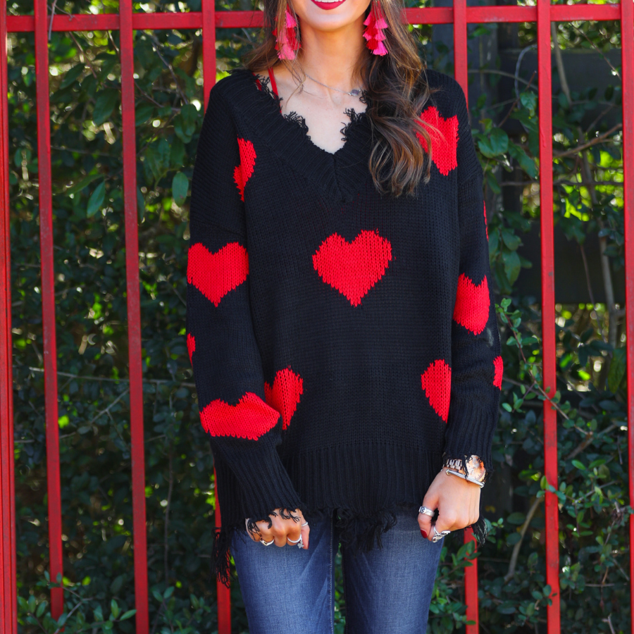 a long-sleeve sweater crafted from ultra soft, stretchy knit fabric with striking red heart motifs across a rich black knit, a relaxed drop-shoulder fit, and distressed ribbed detailing on v-neckline, cuffs, and hemline