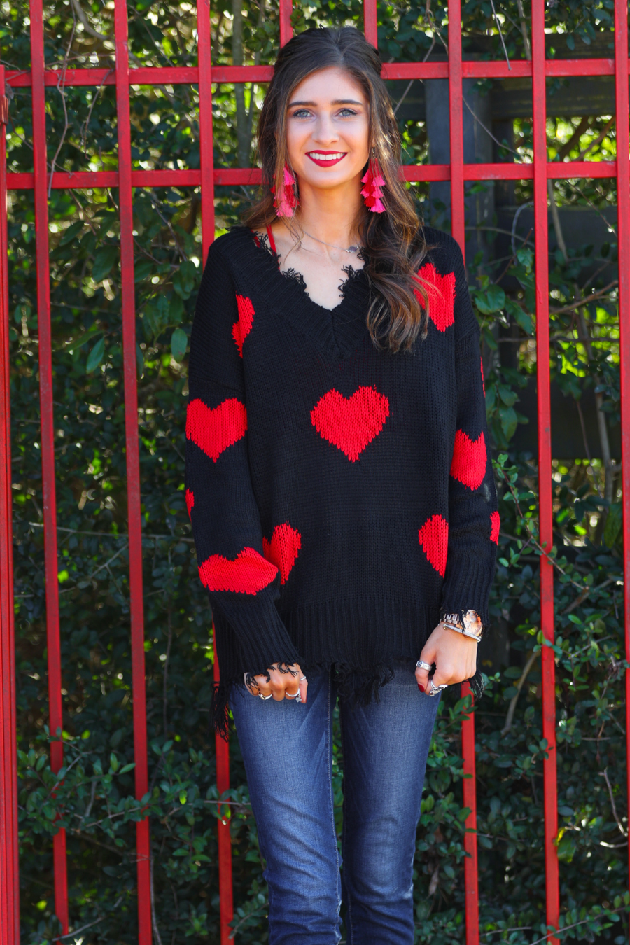a long-sleeve sweater crafted from ultra soft, stretchy knit fabric with striking red heart motifs across a rich black knit, a relaxed drop-shoulder fit, and distressed ribbed detailing on v-neckline, cuffs, and hemline