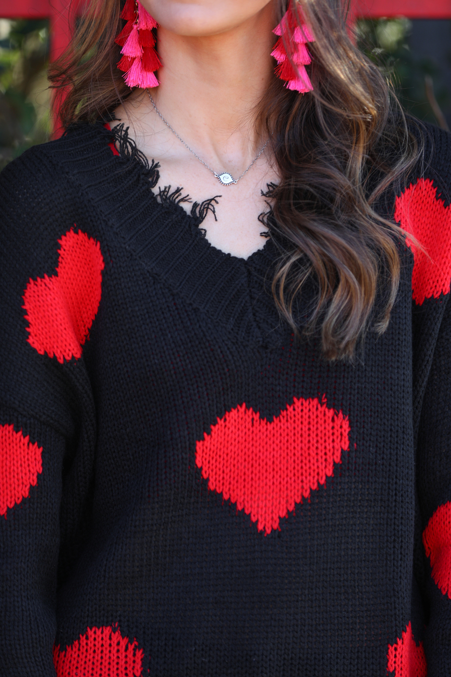 a long-sleeve sweater crafted from ultra soft, stretchy knit fabric with striking red heart motifs across a rich black knit, a relaxed drop-shoulder fit, and distressed ribbed detailing on v-neckline, cuffs, and hemline