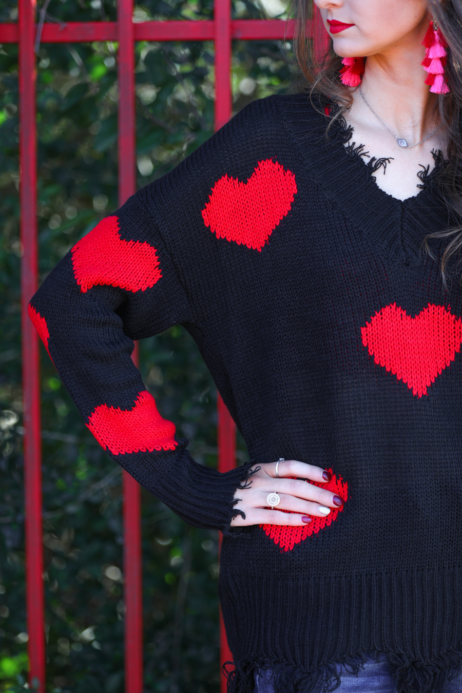 a long-sleeve sweater crafted from ultra soft, stretchy knit fabric with striking red heart motifs across a rich black knit, a relaxed drop-shoulder fit, and distressed ribbed detailing on v-neckline, cuffs, and hemline
