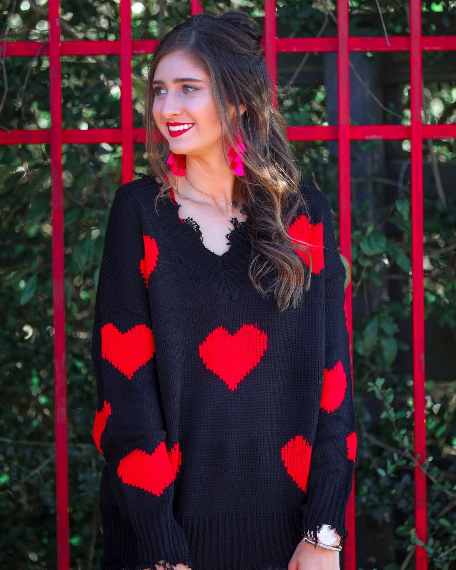a long-sleeve sweater crafted from ultra soft, stretchy knit fabric with striking red heart motifs across a rich black knit, a relaxed drop-shoulder fit, and distressed ribbed detailing on v-neckline, cuffs, and hemline