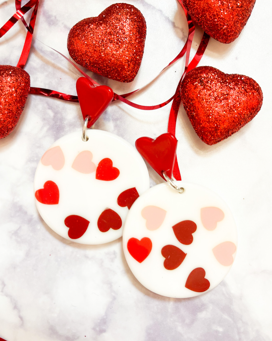 red heart studs accented with dangling acrylic circles and printed hearts in shades of pink and red along with comfort replacement earring backs and plastic disk stopper style in silver