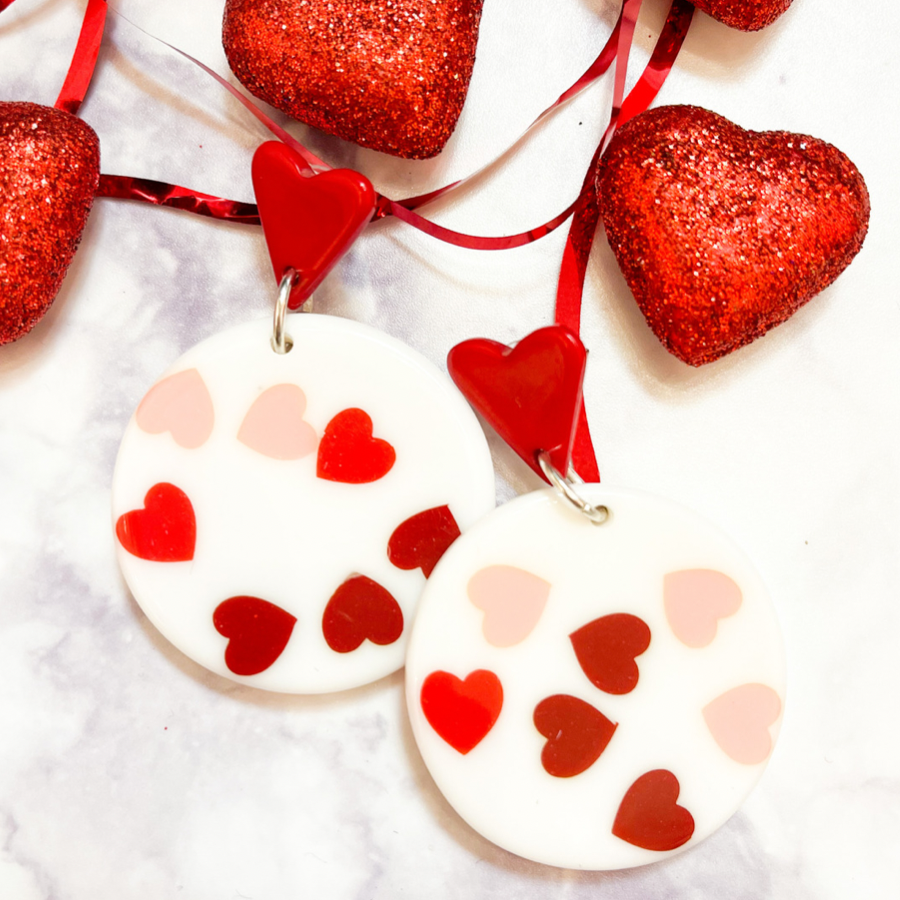 red heart studs accented with dangling acrylic circles and printed hearts in shades of pink and red along with comfort replacement earring backs and plastic disk stopper style in silver