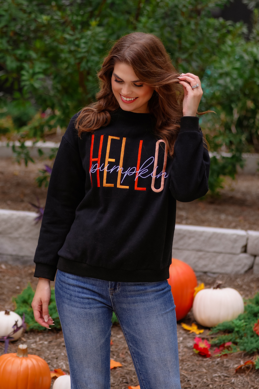 black long-sleeve sweatshirt made of soft mid-weight fabric with a crew neckline, straight hem, and colorful embroidered mix of 'HELLO' in uppercase letters (orange, rose gold, and yellow) and 'PUMPKIN' in white script handwriting