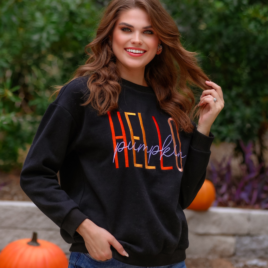 black long-sleeve sweatshirt made of soft mid-weight fabric with a crew neckline, straight hem, and colorful embroidered mix of 'HELLO' in uppercase letters (orange, rose gold, and yellow) and 'PUMPKIN' in white script handwriting