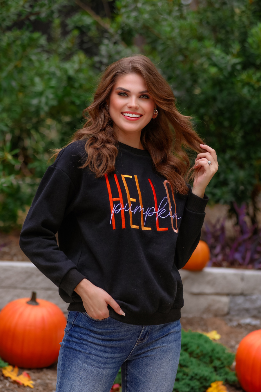 black long-sleeve sweatshirt made of soft mid-weight fabric with a crew neckline, straight hem, and colorful embroidered mix of 'HELLO' in uppercase letters (orange, rose gold, and yellow) and 'PUMPKIN' in white script handwriting